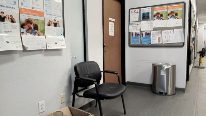 Interior room with informational posters on walls, black chair, trash bin, and doorway to adjacent spaces
