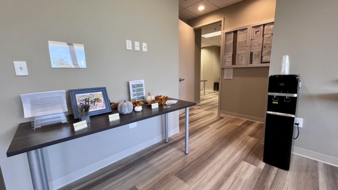 Interior corridor with wood flooring, exit signs, framed nature photography, and clinical lighting throughout facility