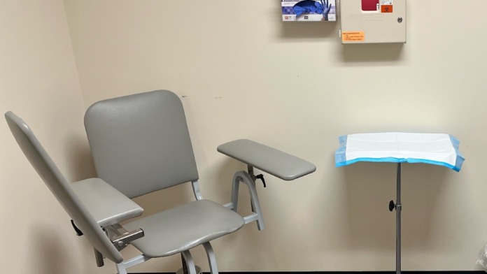Interior treatment room with medical examination chair, supply dispensers, and standard medical furniture