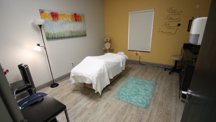 Interior therapy space with massage table, supportive artwork, motivational wall text, and professional treatment equipment