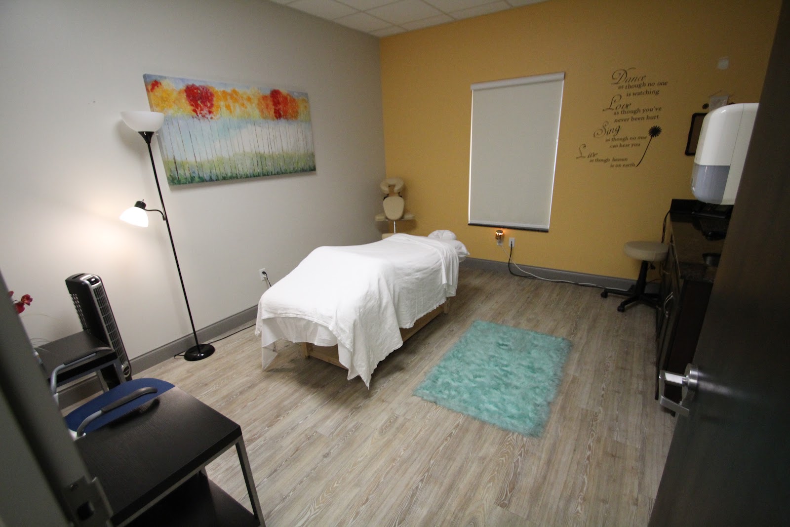 Interior therapy space with massage table, supportive artwork, motivational wall text, and professional treatment equipment
