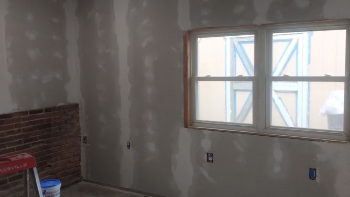 Interior treatment room under renovation with drywall, window with construction tape, and electrical outlets