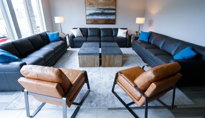 Interior lounge space with black leather sofas, brown leather armchairs, wooden coffee table, artwork, and floor lamps