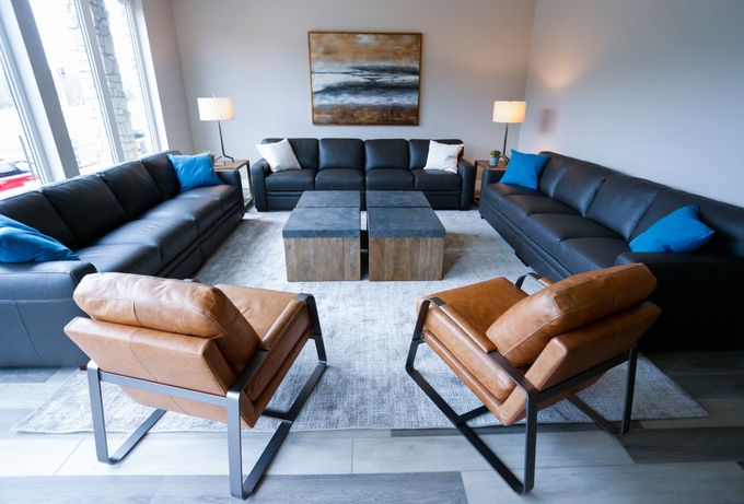 Interior lounge space with black leather sofas, brown leather armchairs, wooden coffee table, artwork, and floor lamps