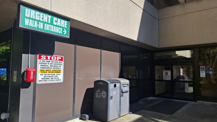 Exterior entrance showing green urgent care walk-in sign, emergency phone, and facility entrance doors