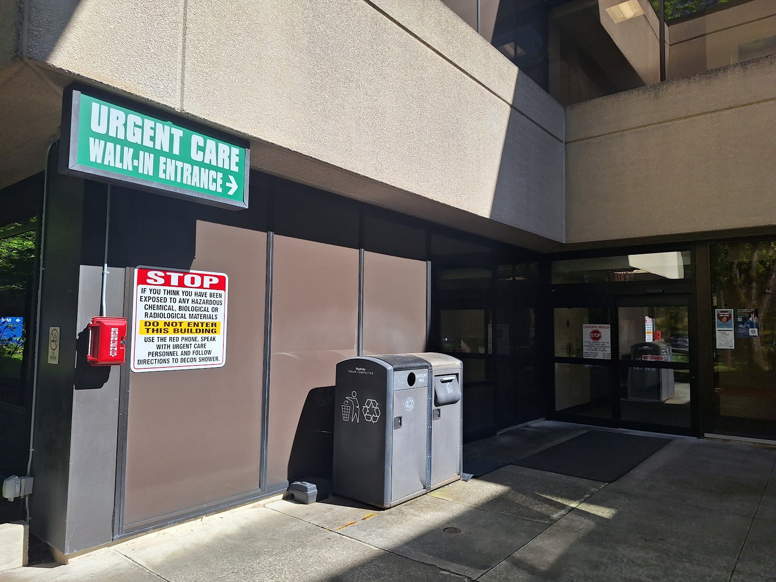 Exterior entrance showing green urgent care walk-in sign, emergency phone, and facility entrance doors