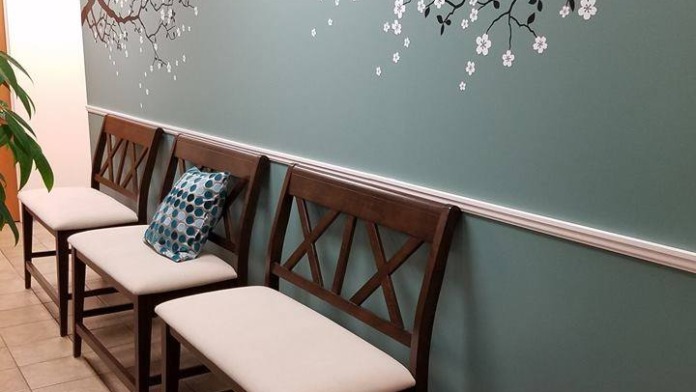 Interior waiting space with chairs along wall decorated with painted floral branch mural and potted plant
