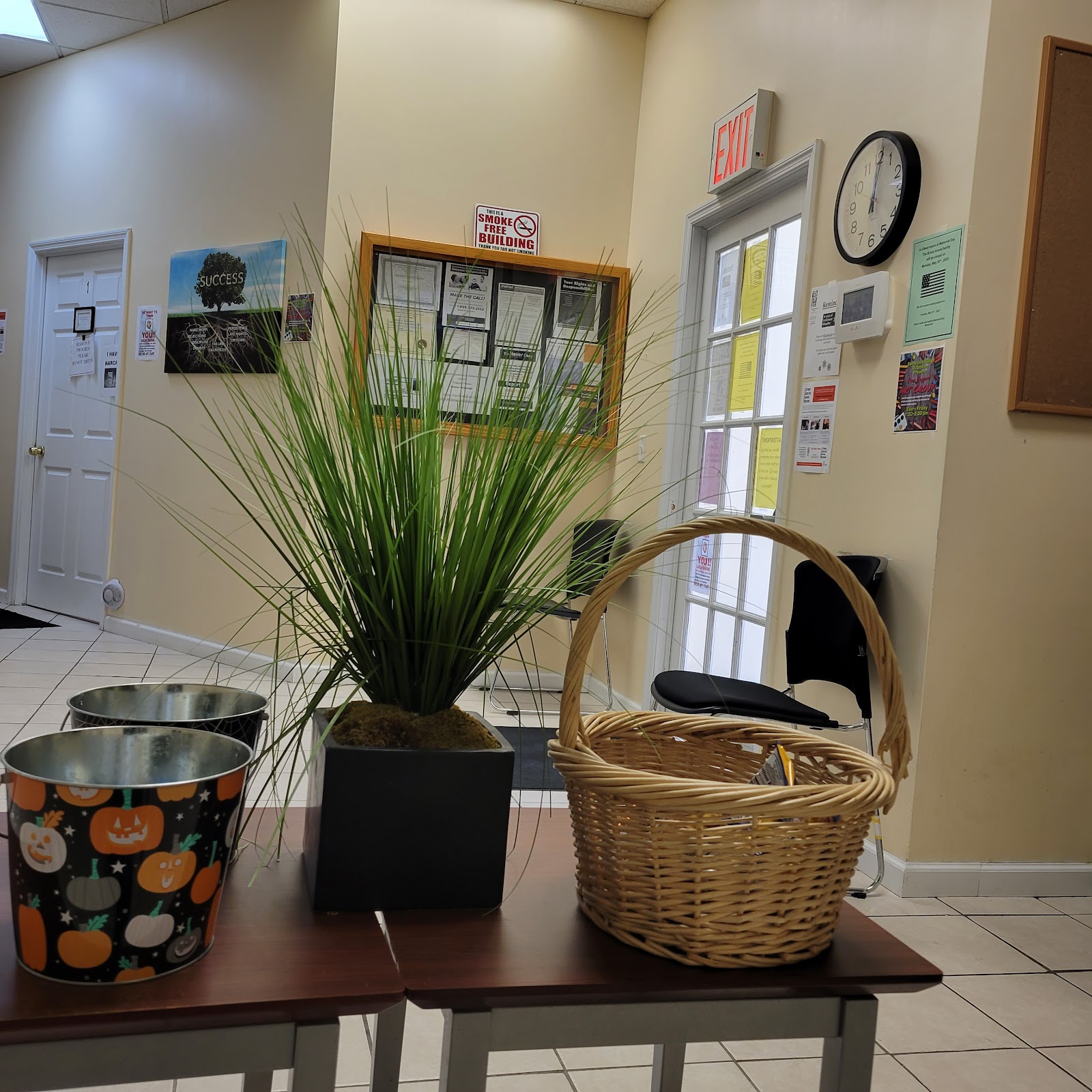 Interior waiting space featuring seating, green plant arrangement, wall-mounted informational signs and clock