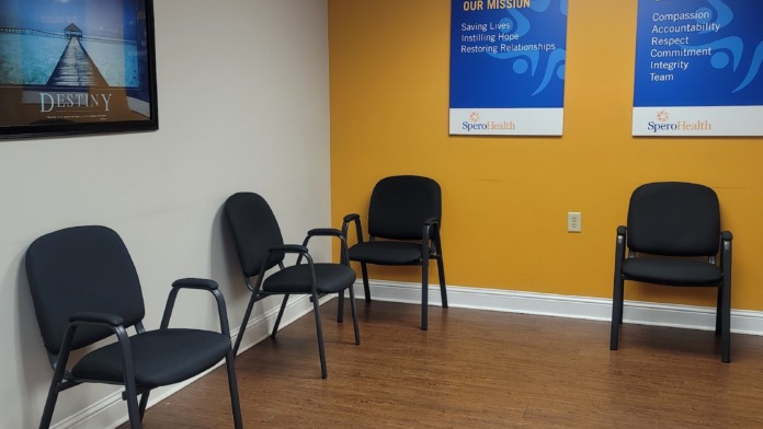 Interior waiting room featuring yellow walls, blue mission and values signage, black chairs, and motivational poster with wooden flooring