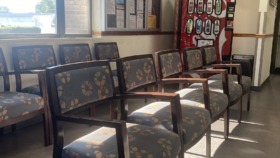 Interior waiting room with multiple upholstered chairs, large window, vending machine, and information boards on wall
