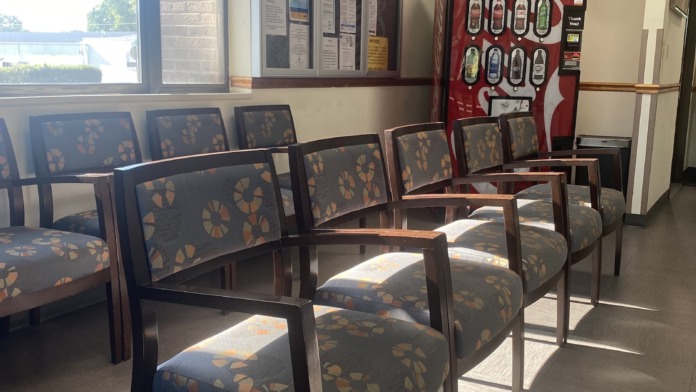 Interior waiting room with multiple upholstered chairs, large window, vending machine, and information boards on wall