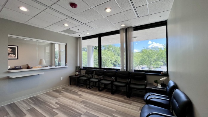 Interior waiting area with black leather seating, large windows overlooking outdoor landscape, reception window visible