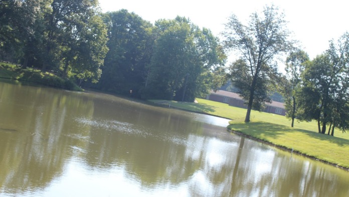 Exterior view of facility grounds featuring pond, mature trees, and green lawn areas