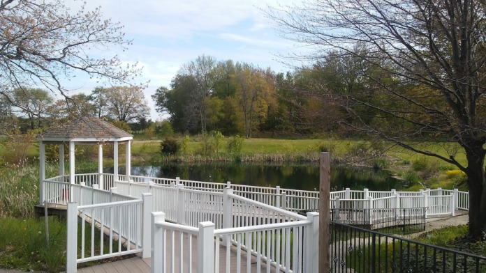 Exterior outdoor space featuring white gazebo pavilion and wooden boardwalk overlooking pond with landscaped grounds