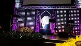 Interior stage with purple and teal lighting, welcome signage, and professional event setup