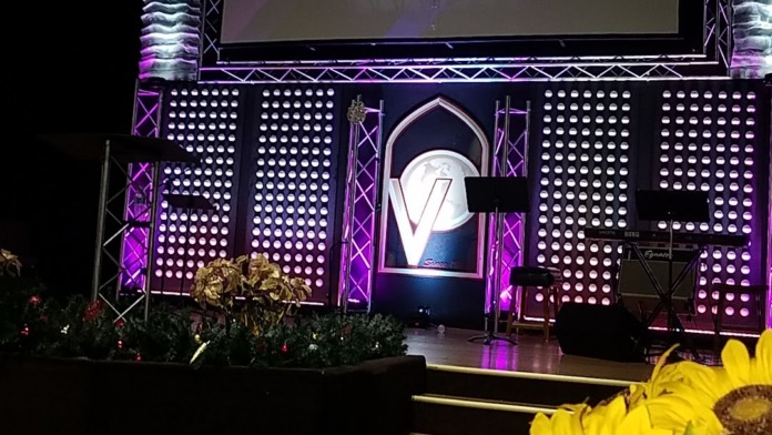 Interior stage with purple and teal lighting, welcome signage, and professional event setup