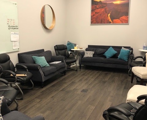 Interior common area with multiple black leather sofas and chairs, wood flooring, landscape artwork, and accent décor.