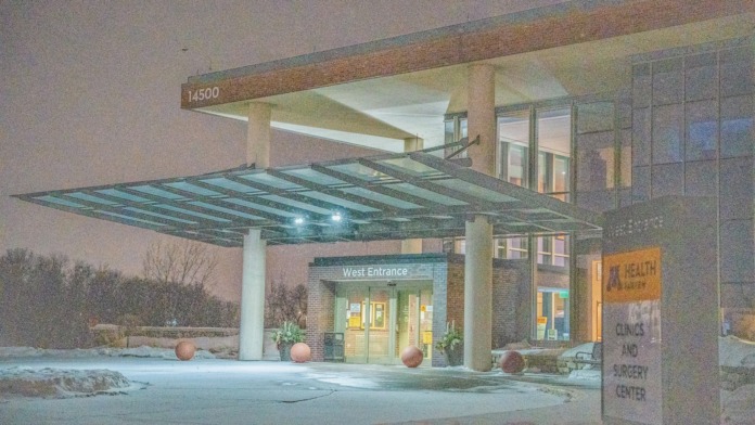Exterior west entrance with glass canopy, illuminated entry doors, brick facade, and nighttime lighting in winter conditions