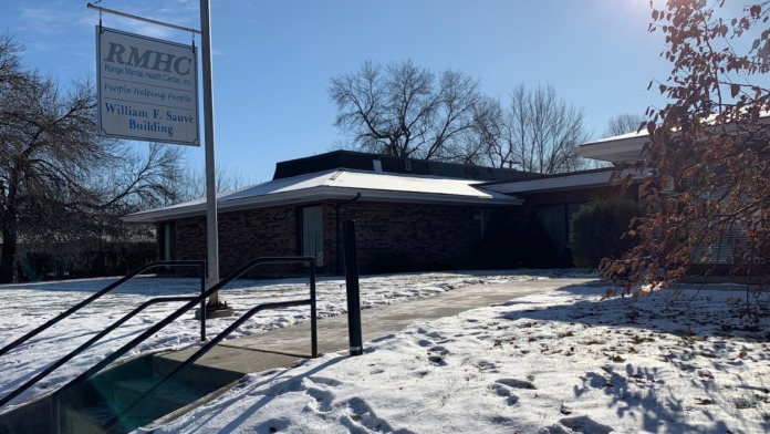 Exterior view of modern mental health facility building with covered shelter structure, parking area, and pole signage