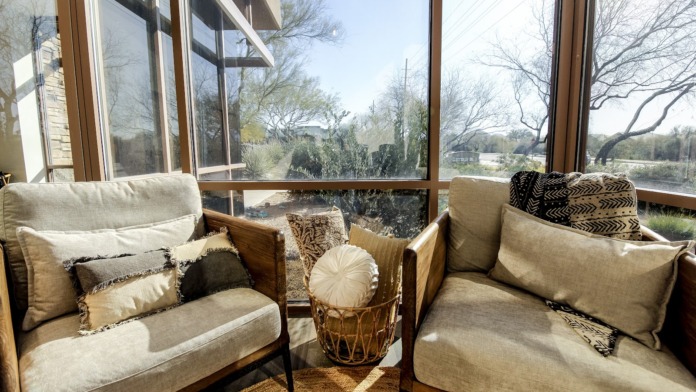Interior seating area with upholstered armchairs, patterned pillows, and large windows overlooking landscaped grounds.