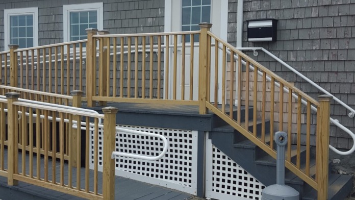Exterior showing wooden accessibility ramp with railings, entrance deck, and building exterior with windows and mailbox
