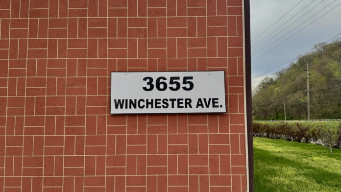 Exterior parking area with accessible parking spaces marked, red brick building facade, metal entrance door, and facility driveway