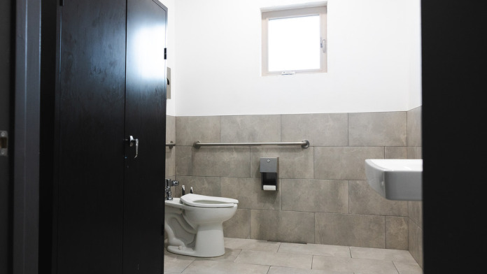 Interior accessible bathroom with toilet, grab bars, sink, window, and beige tile surfaces meeting ADA standards