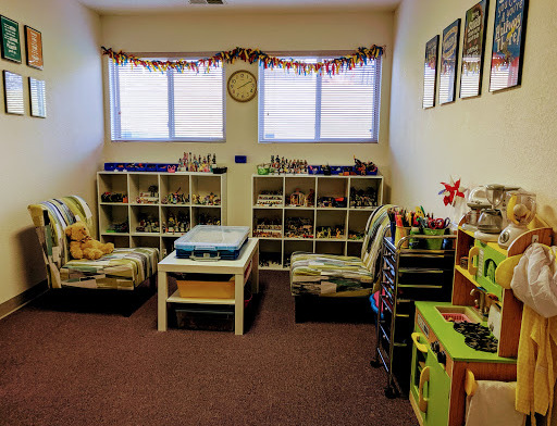Interior room with colorful shelving units containing toys and activities, child-sized furniture, and seasonal window decorations.