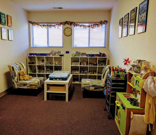 Interior room with colorful shelving units containing toys and activities, child-sized furniture, and seasonal window decorations.