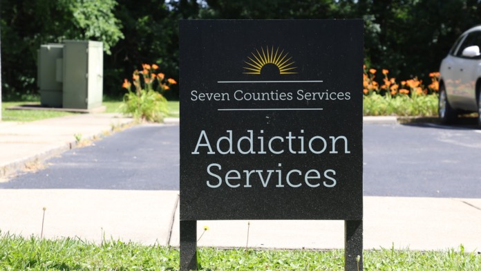 Exterior parking area with Seven Counties Services Addiction Services directional sign, landscaped grounds with flowering plants