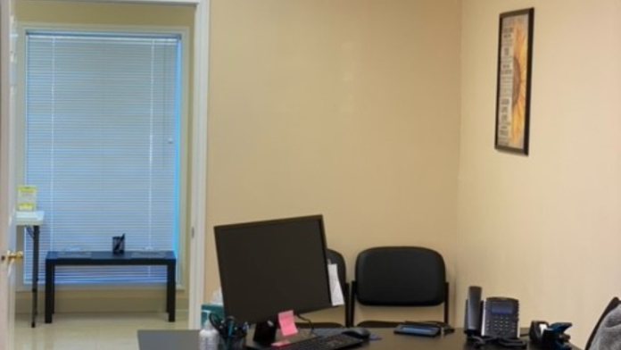 Interior office with desk workstations, office chairs, computer equipment, exit sign, and access to waiting area