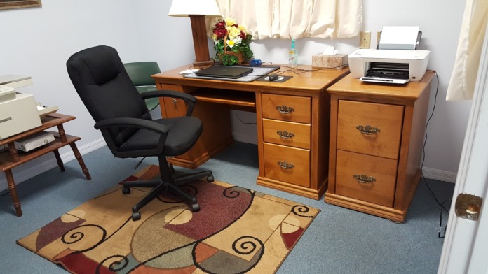 Interior office with wooden desk, black office chair, lamp, computer, and filing cabinets