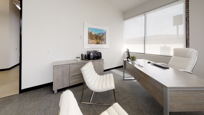 Interior office with desk, office chair, window views, framed landscape photo, and natural lighting