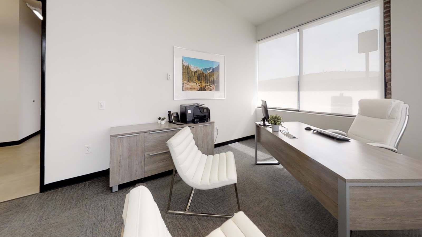 Interior office with desk, office chair, window views, framed landscape photo, and natural lighting
