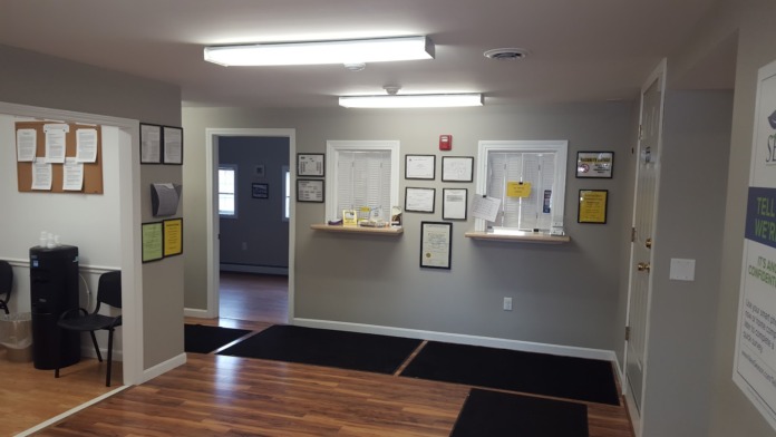Interior administrative space with service counters, office supplies, framed credentials, informational signage, and patient waiting area