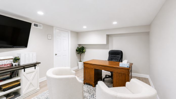 Interior office space with wooden desk, black office chair, wall-mounted television, white shelving, potted plant, and professional workspace setup