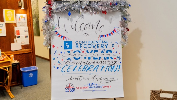 Handwritten welcome poster with tinsel garland announcing Confidential Recovery event and Veterans Navigation Center.