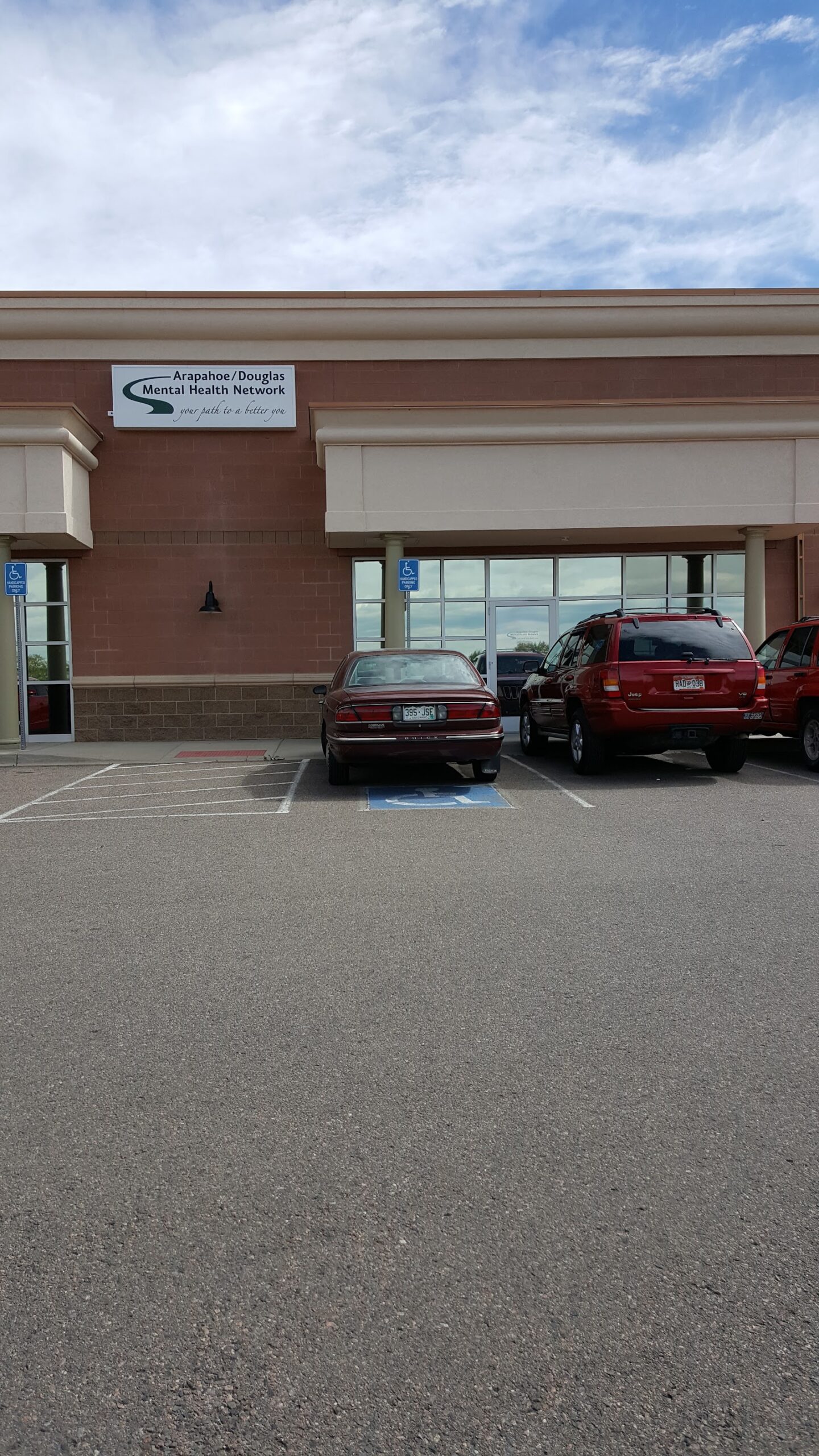 Exterior facility showing Mental Health Network signage, brick construction, glass windows, and parked vehicles