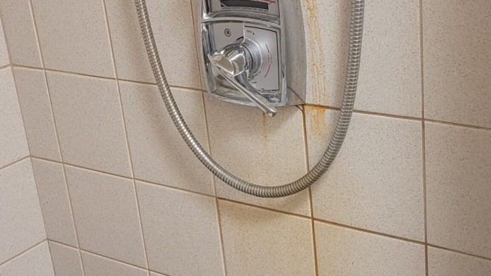 Interior bathroom shower wall with beige tile, dual showerheads, grab bars, and chrome fixtures for accessibility.