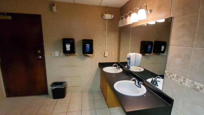 Interior bathroom with dual sink vanity, mirror, soap dispensers, and tile flooring and walls in neutral tones