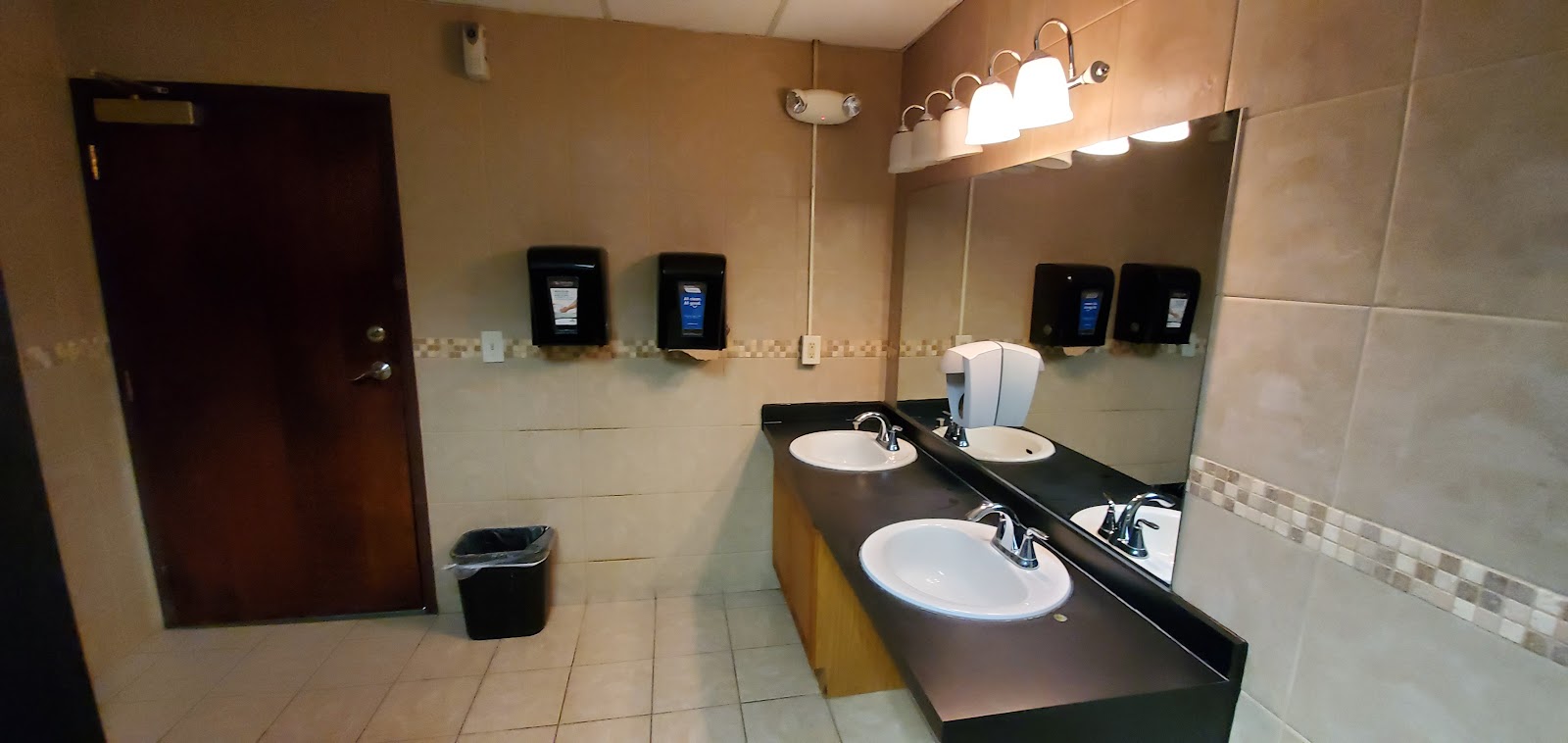 Interior bathroom with dual sink vanity, mirror, soap dispensers, and tile flooring and walls in neutral tones