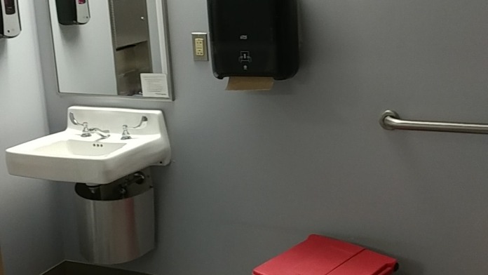 Interior bathroom featuring wall-mounted sink, mirror, paper towel dispenser, and grab bars for accessibility