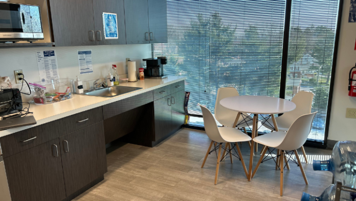 Interior break room with dark cabinetry, white counters, stainless sink, round dining table, and windows