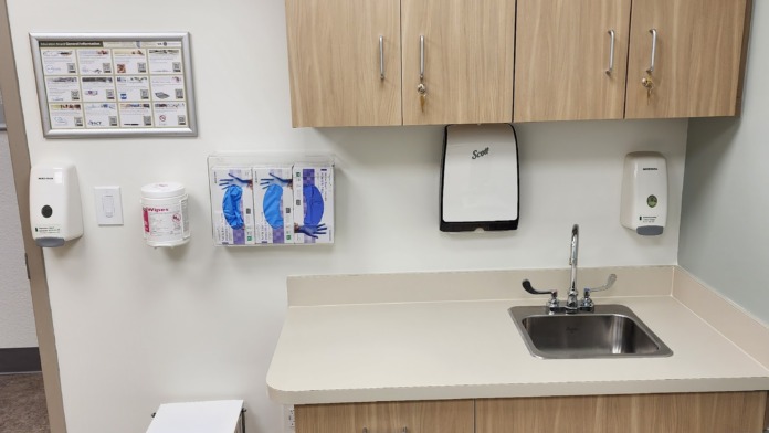Interior break room featuring stainless steel sink, wooden cabinetry, wall-mounted dispensers, supplies, and educational information board