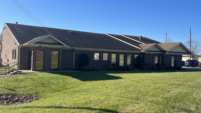 Exterior brick building facade with multiple windows, green lawn, and clear blue sky
