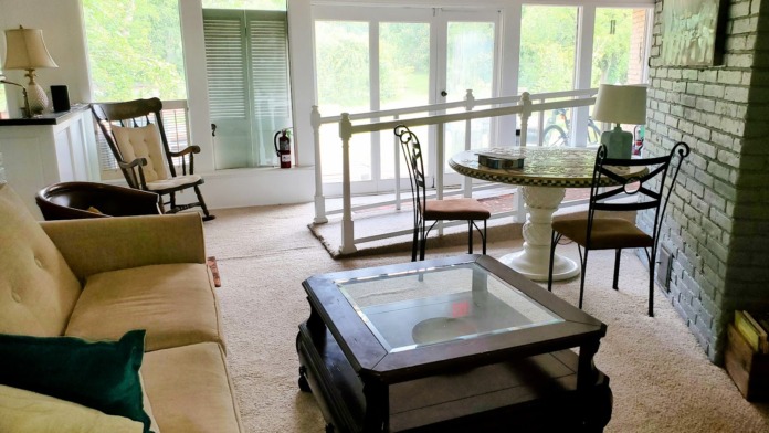 Interior sunroom with large glass doors, brick fireplace, comfortable seating, and natural outdoor views