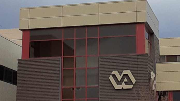 Exterior architectural detail of modern medical building corner showing tan panels, dark accent band, and gridded windows