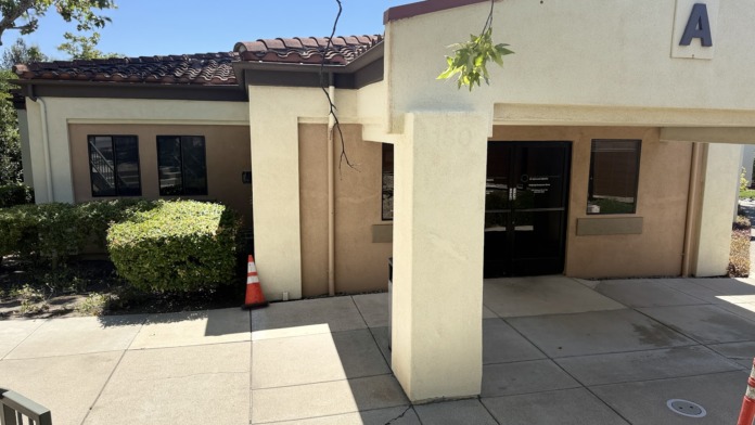 Exterior front entrance of facility unit A-130 with tan stucco walls, dark roof, landscaping, and covered entryway