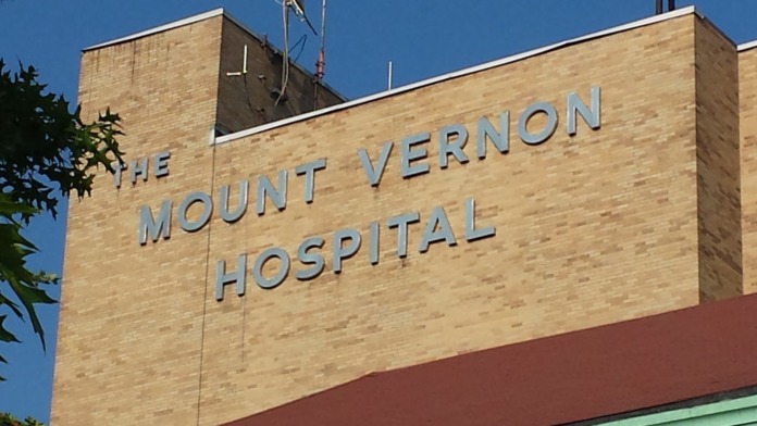 Exterior brick wall with large blue letters reading The Mount Vernon Hospital and rooftop antenna