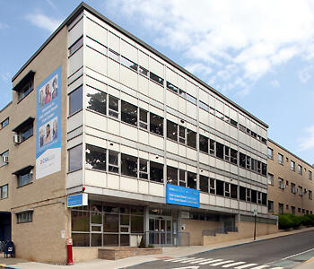 Street-level exterior view of modern healthcare facility with brick facade, aluminum detailing, and blue entrance signage